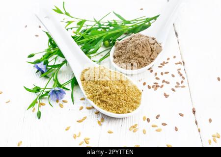 Flachskleie und Mehl in zwei Löffeln, Leinsamen, Blättern und Blumen auf dem Hintergrund eines Holzbretts Stockfoto