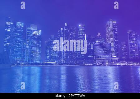 Die Skyline von Singapur bei Nacht, Wolkenkratzer von Unternehmen in Neonfarben, Bürogebäude mit Reflexion im Wasser Stockfoto