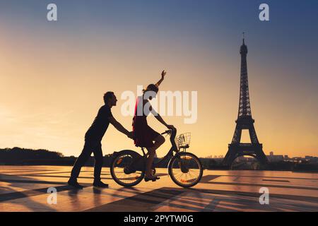 Glückliches Paar, das Spaß in Paris hat und Fahrrad in der Nähe des Eiffelturms und Silhouetten fährt Stockfoto