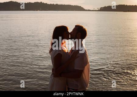 Liebe, Silhouette von Paaren, die sich bei Sonnenuntergang am Strand küssen, Hintergrund für Flitterwochen-Reisen Stockfoto