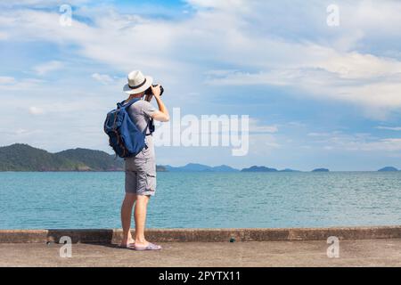 Reisefotograf, männlicher Reisender, der ein Foto vom Meer macht und einen Rucksack trägt, unbekannte Touristenfotografie Stockfoto