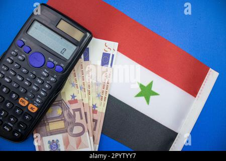 Die syrische Flagge auf blauem Hintergrund, Euro und ein Taschenrechner darauf. Von oben fotografiert. Stockfoto