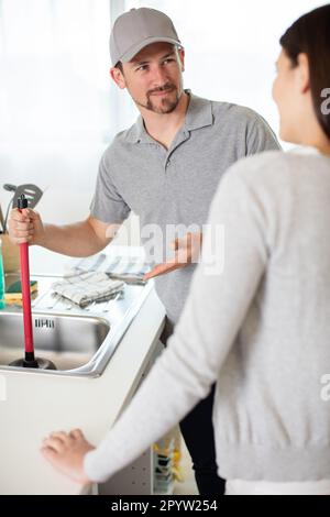 Eine Frau, die einen Klempner ansieht und ein verstopftes Waschbecken reinigt Stockfoto