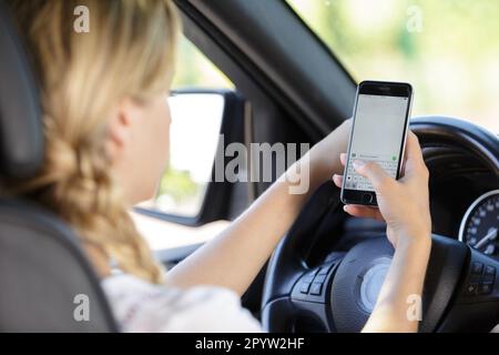 Junge, schöne Frau, die Auto fährt, während sie SMS schreibt Stockfoto