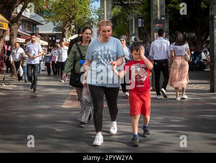 In der belebten Stadt Antalya in der Türkei weint ein kleiner Junge, während seine Mutter seine Hand hält und sie durch eine überfüllte Einkaufsstraße laufen, wie im späten A Stockfoto