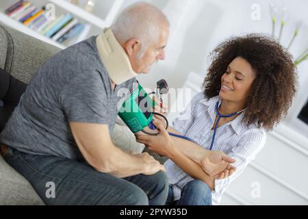 Pflegekraft, die den verletzten Mann zu Hause besucht und den Blutdruck misst Stockfoto
