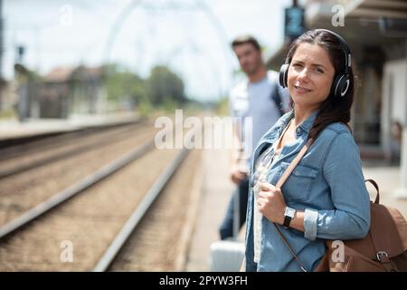 Eine Frau, die am Bahnhof auf den Zug wartet und Musik hört Stockfoto