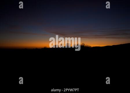 Silhouette von Bäumen auf dem Hügel bei Sonnenuntergang mit Himmel in sanften Farben in Magenta, Pink und Blau horizontal Stockfoto