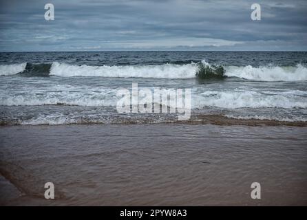 Stürmische Wellen stürzen an einem bewölkten Tag am Ufer eines britischen Strandes ab. Stockfoto