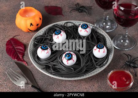 Schwarze Halloween-Pasta dekorierte Horroraugen auf grauem Teller auf braunem Hintergrund Stockfoto