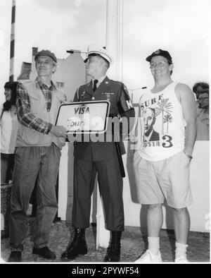 Berlin, Checkpoint Charlie, Friedrichstraße. Am 22. Juni 1990 wurde der Kontrollpunkt im Rahmen einer Gedenkfeier (Militärzeremonie) aufgelöst. Ein Passant hält das zuvor abgemauerte Schild „Visa Tourist“ vor einem amerikanischen Grenzschutz. Schwarz-Weiß. Foto, 06-22-1990." Stockfoto