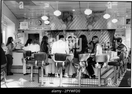 Miami, Florida (USA). Gastronomie, Bar: Gäste sitzen auf Barhockern in der Bar in einer Johnny Rockets Burger Bar in Coconut Grove. Innenansicht, schwarz-weiß. Foto, 1995. Stockfoto
