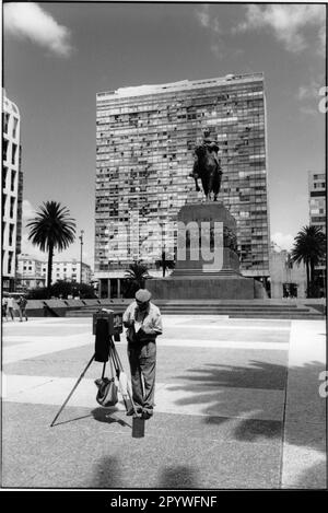 Montevideo (Uruguay). Blick von Nordosten auf die Plaza Independencia. Vorderseite: Fotograf mit Nummernschildkamera. Mitte: Denkmal für José Artigas: Artigas, José Gervasio, uruguayischer Unabhängigkeitskämpfer. 6/19/1774 Montevideo - 9/23/1850 Asunsión (im Exil). Hinten: Hochhaus mit Wohnungen. Schwarz-Weiß. Foto, 1997. Stockfoto