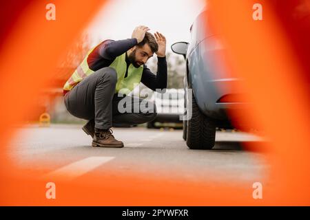 Ein Mann steht neben seinem formell gekleideten Auto und sieht besorgt aus wegen des Motorproblems. Stockfoto