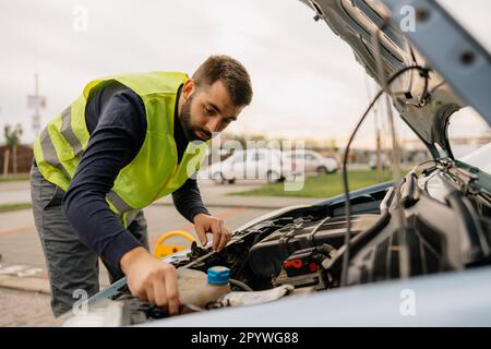 Ein Mann steht neben seinem formell gekleideten Auto und sieht besorgt aus wegen des Motorproblems. Stockfoto