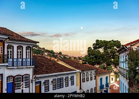 Alte Häuser im Kolonialstil mit Balkonen in der traditionellen historischen Stadt Ouro Preto bei Sonnenuntergang mit dem Mond im Hintergrund, Brasilien Stockfoto