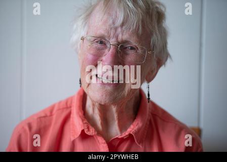 Eine ältere Frau in den 90s Jahren, die ein orangefarbenes Hemd trägt, das von der Seite mit natürlichem Licht beleuchtet wird. Stockfoto