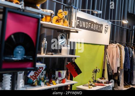 05. Mai 2023, Baden-Württemberg, Freiburg: Ein Schild mit der Aufschrift "Fundfabrik" hängt am Stand der Abfallwirtschaft u. Stadtreinigung Freiburg GmbH (ASF) auf der Nachhaltigkeits-Messe "Greenflair". Im nächsten Jahr soll der neue Second-Hand-Laden Fundfabrik der ASF eröffnet werden. Das Konzept ist „einzigartig“, neben einer ausgewählten Auswahl an gebrauchten Möbeln, Möbeln, Haushaltsartikeln und gebrauchter Bekleidung bietet die Fundfabrik ihren Gästen auch „Upcycling-Workshops“, einen „Reparaturworkshop“ und Bildungsmöglichkeiten zu den Themen Nachhaltigkeit und Kreislaufwirtschaft an. Die neue Buil Stockfoto