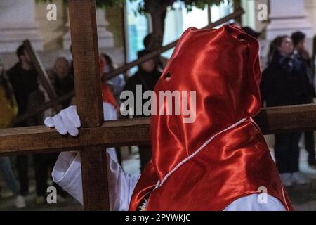 Eine mit Kapuze versehene Buße läuft barfuß mit Ketten, während er ein hölzernes Kreuz trägt, während der Mitternachtsstummprozession, die Karfreitag in der Heiligen Woche oder Semana Santa am 6. April 2023 in Ronda, Spanien, markiert. Ronda, die sich im 6. Jahrhundert v. Chr. niedergelassen hat, hält seit über 500 Jahren Heilige Woche-Prozessionen ab. Stockfoto