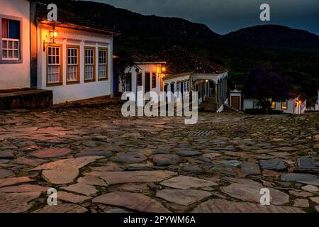 Straßen und Häuser der historischen Stadt Tiradentes beleuchtet in der Dämmerung mit den Bergen im Hintergrund, Brasilien Stockfoto