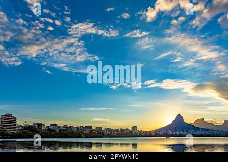 Sonnenuntergang in der Lagune Rodrigo de Freitas mit den Gebäuden und Hügeln der Stadt Rio de Janeiro, die sich im Wasser, Brasilien, spiegeln Stockfoto