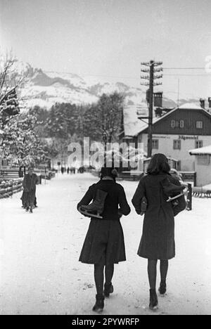 Zwei junge Frauen laufen durch St. Johann. Ihre Schlittschuhe hängen über ihren Schultern. Unbefriedigtes Bild, wahrscheinlich im Winter 1938/39. Stockfoto