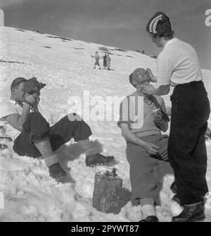 Ein Make-up-Künstler schminkt einen Schauspieler für die Schießerei. Dahinter filmt ein Kameramann die Szene. Die Aufnahmen stammen wahrscheinlich aus der Mitte der 1930er Jahre und stehen im Zusammenhang mit den Olympischen Winterspielen 1936 in Garmisch-Partenkirchen. Stockfoto