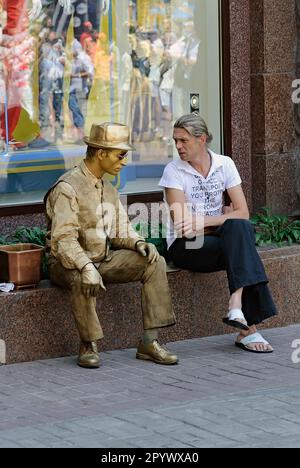 Ein unidentifizierter Passant chattet mit einem unidentifizierten, faulen Pantomime, der in der Chreshchatyk Street in Kiew, Ukraine auftritt Stockfoto