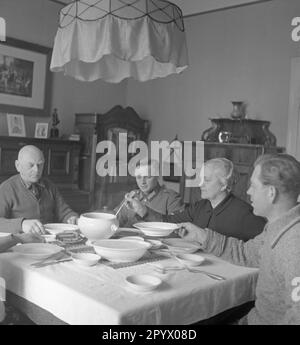 Fünf Leute sitzen an einem überdachten Esstisch, wahrscheinlich auf einer Farm in der Nähe von Neustrelitz. Eine Frau verteilt Essen aus einer Suppenschüssel. Unbefristetes Foto. Stockfoto