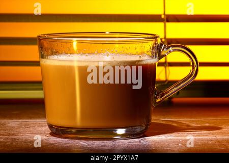 Glas-Kaffeetasse gefüllt mit Kaffee Set vor einem Küchenfenster-Jalousien Stockfoto