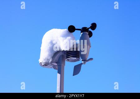 Die Sensoren der Wetterstation für zu Hause sind mit Schnee bedeckt, vor dem blauen Winterhimmel Stockfoto