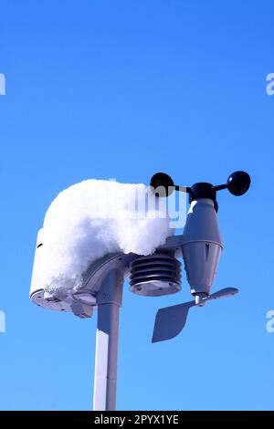 Die Sensoren der Wetterstation für zu Hause sind mit Schnee bedeckt, vor dem blauen Winterhimmel Stockfoto