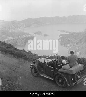 Touristen genießen den Blick auf die Bucht von einer erhöhten Straße. Unbezahlter Schuss, wahrscheinlich in Ponta Delgada auf der Insel Sao Miguel in den 1930er Jahren gemacht. Stockfoto