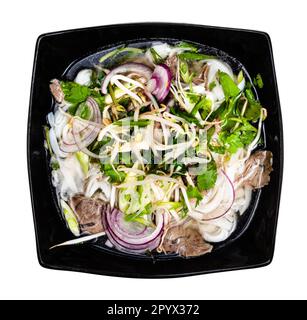 Blick von oben auf vietnamesische Suppe Pho Bo mit Reisnudeln, Brühe, Zwiebeln, Gemüse, Rindfleisch in der Schüssel, Ausschnitt auf weißem Hintergrund Stockfoto