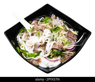 Vietnamesische Suppe Pho Bo mit Reisnudeln, Brühe, Zwiebeln, Gemüse, Rindfleisch in der Schüssel mit Keramiklöffel-Ausschnitt auf weißem Hintergrund Stockfoto