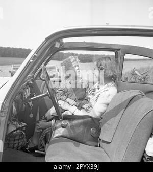 Ein Mädchen sitzt in einem Auto auf dem Schoß einer Frau, die auf dem Beifahrersitz sitzt. Stockfoto