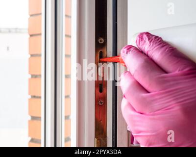 Hand in rosa Handschuh schmiert Fensterrahmen in Nahaufnahmen von städtischen Wohnungen aus Ölkanister Stockfoto