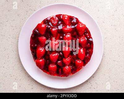 Blick von oben auf süßen Kuchen mit Erdbeeren und Kirschen auf rosa Teller und pinkfarbenem Steinbrett Stockfoto