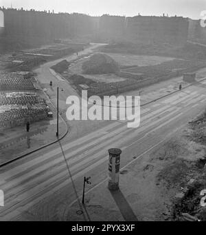 Undatiertes Foto einer Straße in Berlin, vermutlich Westberlin, 1950, mit ausgekleideten verlassenen Bereichen. Auf der linken Straßenseite, Steine, um neue Häuser zu bauen. Im Vordergrund, Straßenschilder, Laternen und eine Plakatwand mit Plakaten. Am Horizont, teilweise zerstörte Wohnblöcke. Stockfoto