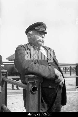 Undatiertes Foto eines Bauern mit einer Spitzmütze (lehnt sich an ein Tor) auf dem Viehmarkt in Husum um 1940. Stockfoto