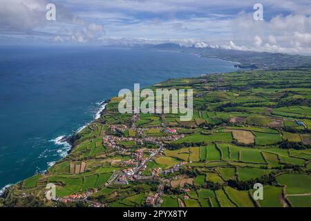 Luftaufnahme der Küste auf der Insel Sao Miguel mit Stadtgebäuden, grünem Ackerland und vulkanischen Bergen, Azoren, Portugal Stockfoto