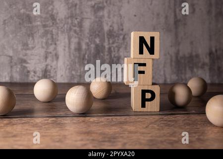 Text NFP - nicht-landwirtschaftliche Gehaltsabrechnungen - auf Holzblöcken im Hintergrund von Finanzdiagrammen. Stockfoto