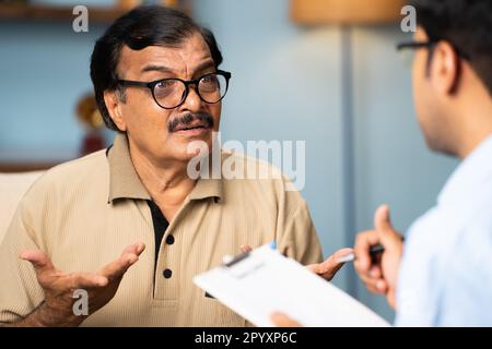 Indische Bankerin, die Zeichen von Seniorenfrau nimmt, indem sie zu Hause Geld spendet - Konzept der finanziellen Hilfe, Investition und Altersversorgung Stockfoto