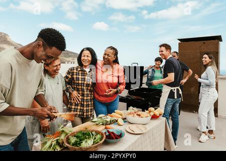 Glückliche, generationenübergreifende Menschen, die Spaß beim Grillen auf dem Dach des Hauses haben - Sommerversammlungen und Essenskonzept Stockfoto