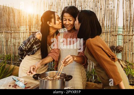 Südostasiatische Mutter und ihre Töchter haben Spaß dabei, gemeinsam auf der Terrasse des Hauses thailändische Gerichte zuzubereiten Stockfoto