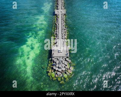 Luftaufnahme eines Seepiers, der sich über das Wasser erstreckt, mit einem Fischer am Ende Stockfoto