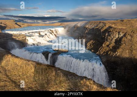 Berühmter Teil des goldenen Kreises. Zwei Kaskaden des Wasserfalls Gullfoss, umgeben von Klippen. Goldene Farbe der Natur am frühen Abend. Gullf Stockfoto