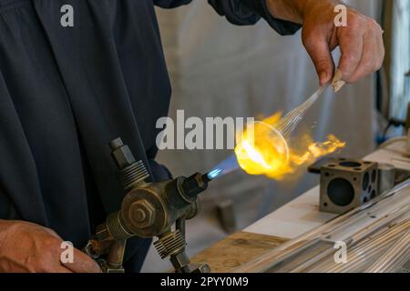 Glasgebläse, die Glas Formen, das durch die Flamme des Brenners erhitzt wird. Stockfoto