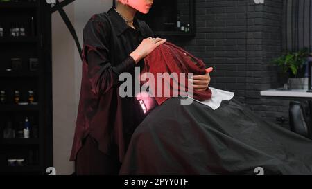 Der Friseur bedeckt das Gesicht des Mannes mit einem heißen Handtuch. Ein Kunde mit einem heißen Handtuch im Gesicht, bevor er sich in einem Friseursalon rasiert Stockfoto