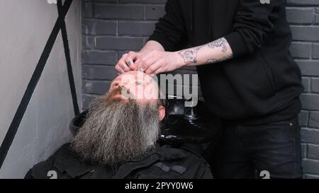Ein Mann entspannt sich, wenn er sich die Haare in einem Friseur wäscht. Der Barbier wäscht den Kopf des Kunden Stockfoto